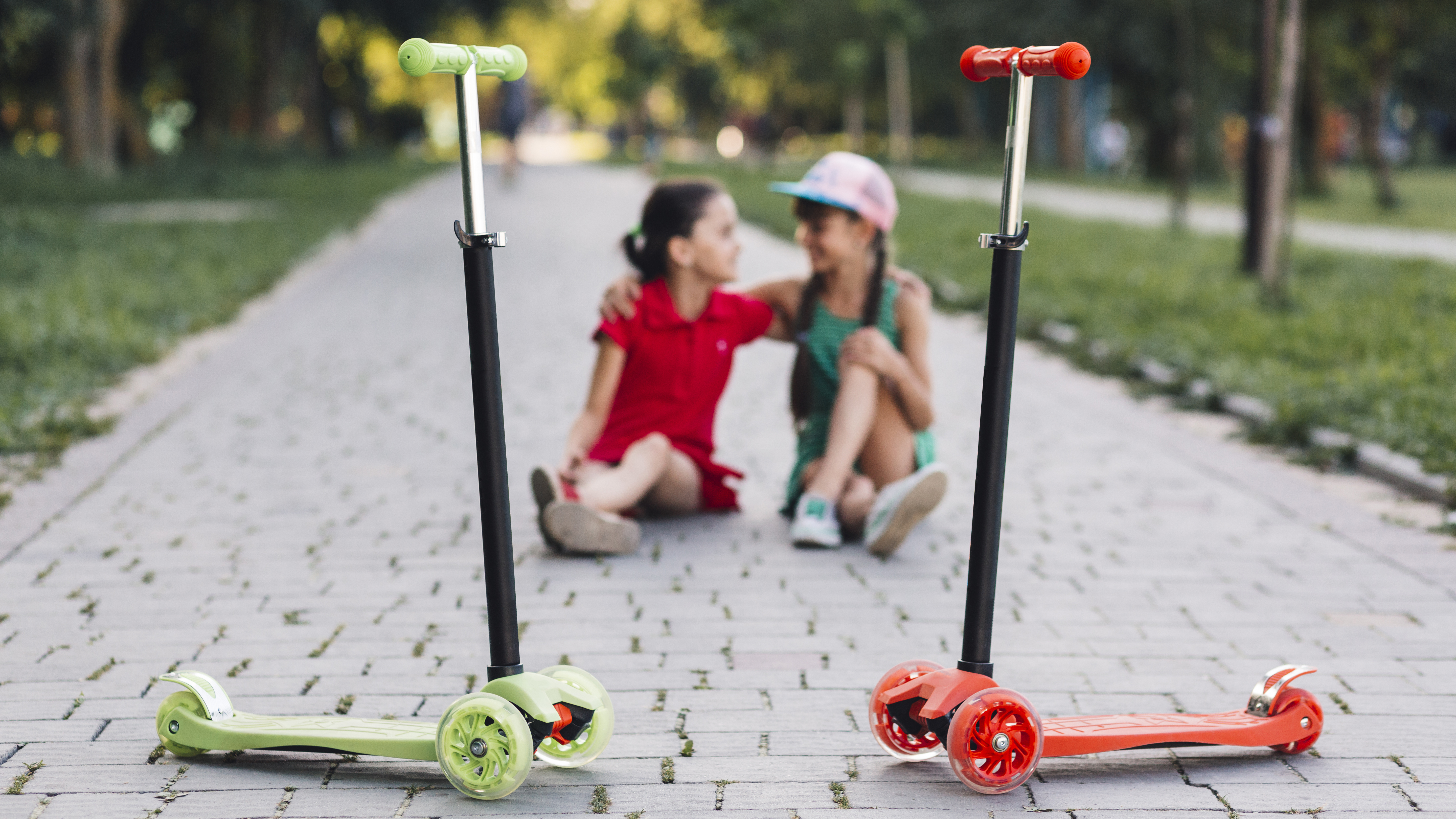 Two children sitting with their scooters in front